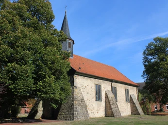 Eine historische Dorfkirche in Münchehagen, umgeben von Bäumen, mit einem markanten Kirchturm.