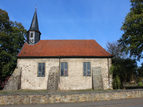 Kirche Münchehagen Historische Kirche Münchehagen mit rotem Ziegeldach und Uhrenturm, umgeben von Bäumen und Steinmauer.