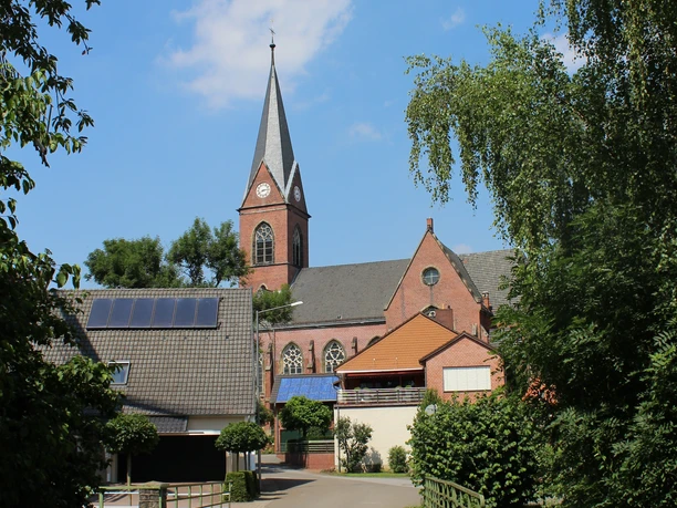 Kirche Lahde Historische Backsteinkirche mit hohem Turm und spitzem Dach umgeben von grünen Bäumen und Gebäuden.