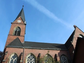 Kirche Lahde Kirche aus rotem Backstein mit hohem Turm und Glocke, umgeben von Bäumen, unter blauem Himmel.