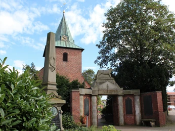 Marienkirche Leeste mit rotem Klinkerturm, spitzem grünen Dach und umliegender Begrünung.