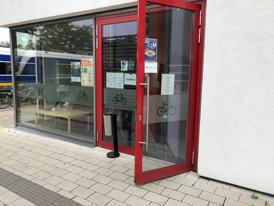 Fahrradstation am Bahnhof Kirchweyhe Fahrradstation am Bahnhof Kirchweyhe mit rotem Eingang, Glasfront und abgestelltem Zug im Hintergrund.
