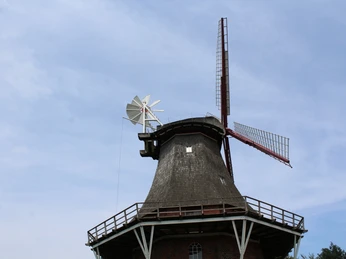 Historische Windmühle in Martfeld mit grauen Holzflügeln und rotem Klinkerbau, bei blauem Himmel.