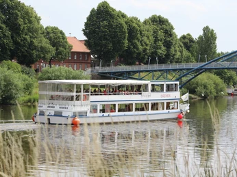 FGS Bremen an der Fußgängerbrücke Ein weißes Ausflugsschiff mit dem Namen "FGS Bremen" fährt in ruhiger Flusslandschaft unter einer Brücke.