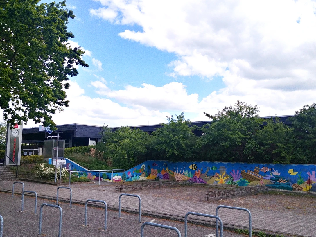 Freibad Weyhe mit farbenfroher Unterwasserwelt-Malerei und üppigem Grün im Hintergrund.