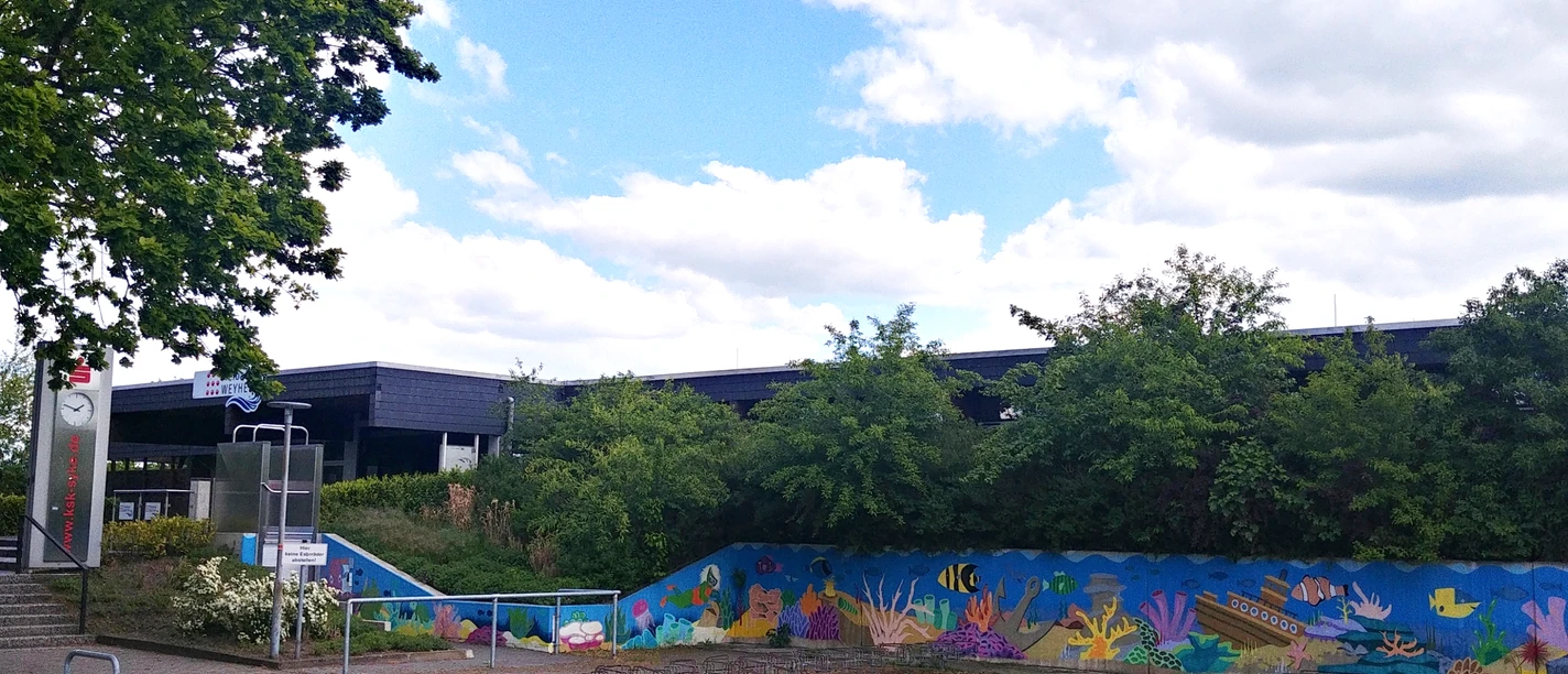 Freibad Weyhe mit farbenfroher Unterwasserwelt-Malerei und üppigem Grün im Hintergrund.
