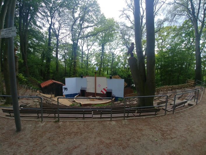 Freilufttheater in einem bewaldeten Gebiet mit Sitzbänken vor einer zentralen Bühne aus Holz.