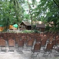 Freilichtbühne Stöckse Freilichtbühne mit leeren Holzbänken im Wald, umgeben von Bäumen und traditioneller Kulisse.