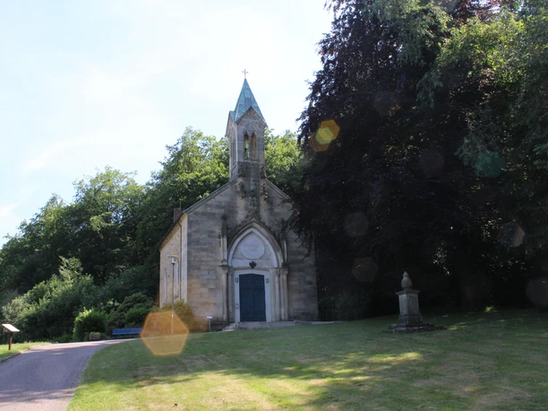 Friederikenkapelle Eine historische Kapelle mit gotischen Elementen, umgeben von üppigem Grün und einem Gedenkstein.