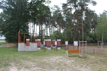 Gedenkstätte in Heemsen mit Informationstafeln vor einem bewaldeten Hintergrund und einer Sitzbank.