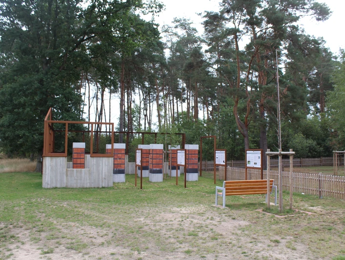 Gedenkstätte in Heemsen mit Informationstafeln vor einem bewaldeten Hintergrund und einer Sitzbank.