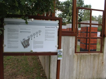 Gedenkstätte mit Informationstafel und Betonwänden, die orangefarbene Ziegel mit Inschriften tragen.