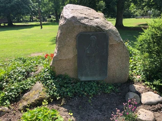Skulptur Gedenkstein Hoppe Gedenkstein mit Bronzetafel in einer grünen Parklandschaft, umgeben von kleinen Blumenbeeten.