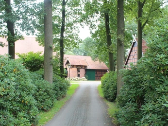 Ein traditionelles Fachwerkgehöft mit Ziegeldach und grünen Toren, umgeben von üppigem Grün.