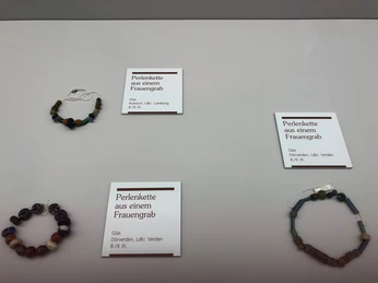 Perlenketten aus Glas aus dem 8./9. Jh., ausgestellt im Landesmuseum Hannover, kreisförmig angeordnet.