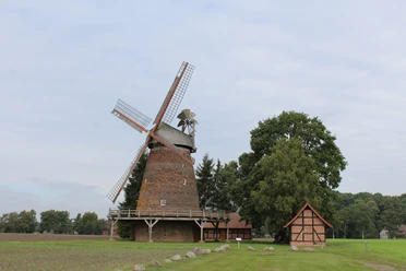 Windmühle Hoyersförde Historische Windmühle Hoyersförde vor bewölktem Himmel, umgeben von Bäumen und einem Fachwerkgebäude.