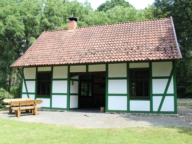 Grüner Jäger Darlaten Fachwerkhaus mit grünem Gebälk und rotem Ziegeldach, umgeben von Bäumen und gepflastertem Weg.