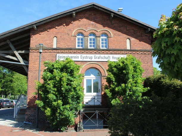 Der Güterschuppen Eystrup aus rotem Backstein mit grüner Bepflanzung vor zwei Rundbogenfenstern.