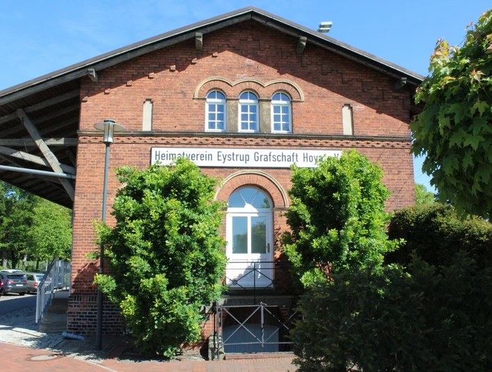 Der Güterschuppen Eystrup aus rotem Backstein mit grüner Bepflanzung vor zwei Rundbogenfenstern.