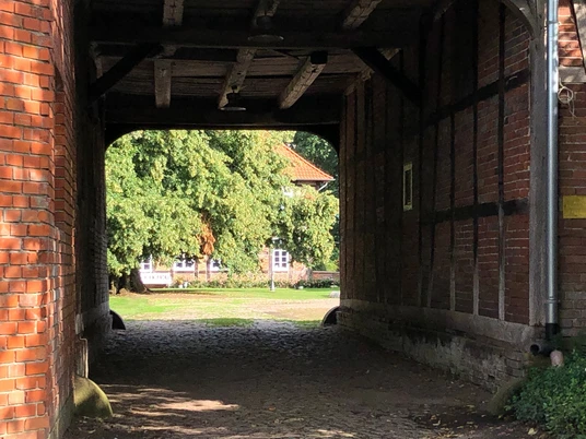 Blick durch ein giebelgedecktes Tor auf einen gepflasterten Hof, umgeben von alten Backsteinwänden.