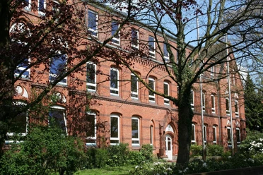 Schule aus roten Ziegeln mit großen Fenstern, umgeben von Bäumen und gepflegtem Grün.