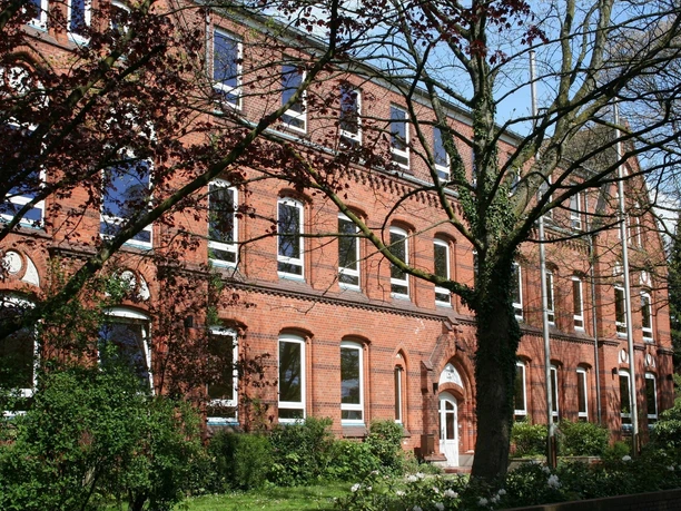 Schule aus roten Ziegeln mit großen Fenstern, umgeben von Bäumen und gepflegtem Grün.