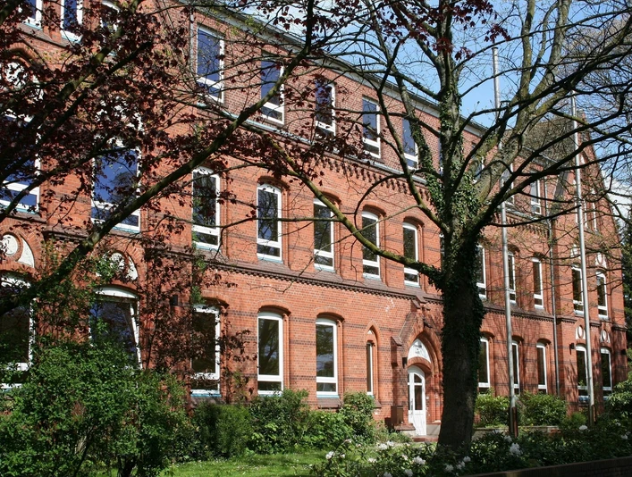Schule aus roten Ziegeln mit großen Fenstern, umgeben von Bäumen und gepflegtem Grün.