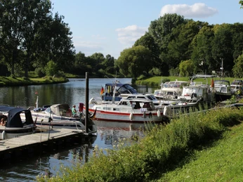 Hafen Nienburg Am Flussufer liegen Boote an einem Holzsteg vertäut, umgeben von üppigem Grün und Bäumen.Boats are moored to a wooden jetty on the riverbank, surrounded by lush greenery and trees.Bådene er fortøjet til en træbrygge på flodbredden, omgivet af frodige grønne områder og træer.Boten liggen aangemeerd aan een houten steiger aan de rivieroever, omringd door weelderig groen en bomen.