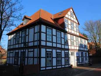 Hakenhof Fachwerkhaus mit roten Ziegeln und blauen Fenstern, umgeben von kahlen Bäumen an einem klaren Tag.