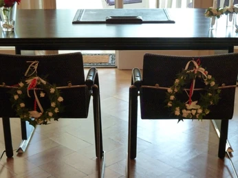 Haus Hünenburg Zwei geschmückte Stühle stehen vor einem dunklen Tisch in einem lichtdurchfluteten Raum.