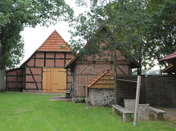 Fachwerkhaus mit Holz- und Backsteinfassade, umgeben von grüner Wiese und alten Bäumen.
