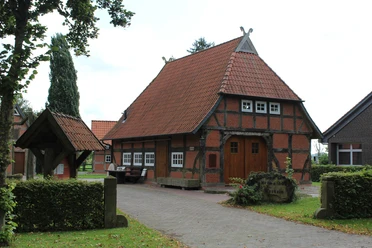 Historisches Fachwerkhaus mit Ziegeldach und Brunnendekor, umgeben von Bäumen in ruhiger Lage.