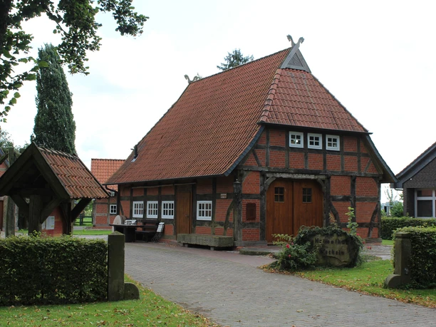 Historisches Fachwerkhaus mit Ziegeldach und Brunnendekor, umgeben von Bäumen in ruhiger Lage.
