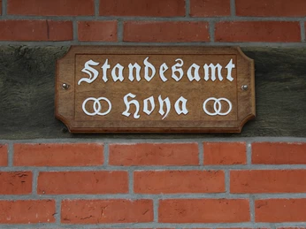 Heimathaus Wechold Holzschild mit der Aufschrift "Standesamt Hoya" an einer Ziegelwand, verziert mit Ringen.