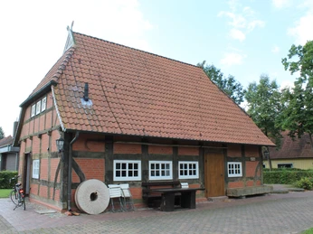 Fachwerkgebäude mit ziegelrotem Dach, umgeben von Bäumen und einem Fahrrad neben der Hauswand.