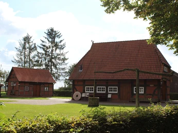 Traditionelles Fachwerkhaus mit rotem Ziegeldach im Grünen, umgeben von Bäumen und Sträuchern.