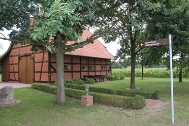 Heimathaus Deblinghausen Fachwerkhaus unter Bäumen, braun-schwarze Balken, im Grünen mit Wegweiser und Sicht auf Felder.