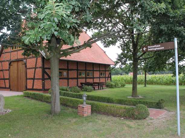 Heimathaus Deblinghausen Fachwerkhaus unter Bäumen, braun-schwarze Balken, im Grünen mit Wegweiser und Sicht auf Felder.