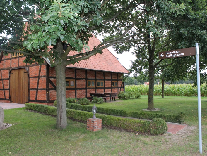 Heimathaus Deblinghausen Fachwerkhaus unter Bäumen, braun-schwarze Balken, im Grünen mit Wegweiser und Sicht auf Felder.