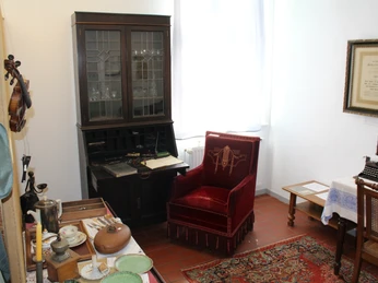 Ein gemütlicher Raum mit antiker Möblierung, darunter ein roter Sessel und eine Glasvitrine.