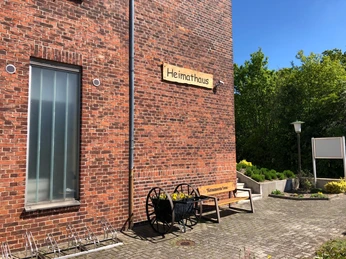 Heimatmuseum Leese: Roter Ziegelbau mit Bank und Rad, umgeben von grünen Bäumen bei blauem Himmel.
