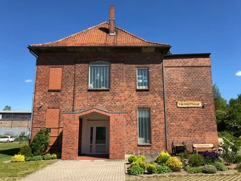 Rotes Backsteingebäude des Heimatmuseums Leese mit grünen Beeten und blauem Himmel im Hintergrund.