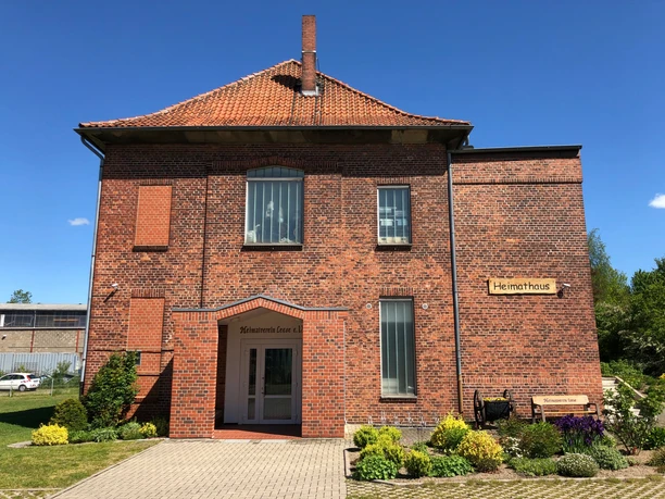 Rotes Backsteingebäude des Heimatmuseums Leese mit grünen Beeten und blauem Himmel im Hintergrund.