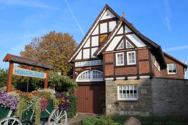 Fachwerkhaus mit Blumenbeet davor, Heimatmuseum Rehburg bei sonnigem Wetter und blauem Himmel.