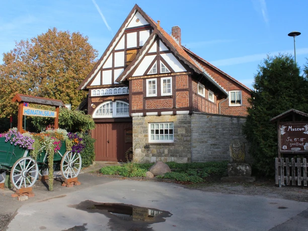 Historisches Fachwerkgebäude mit Blumenkarren im Vordergrund, blauer Himmel im Hintergrund.