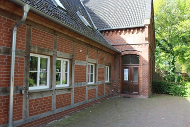 Fachwerkgebäude mit roten Ziegeln und weiß eingerahmten Fenstern in ländlicher Umgebung.