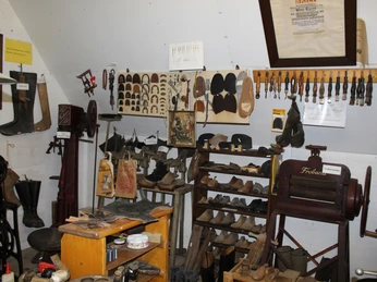 Heimatstube Wietzen Historische Werkstatt mit alten Schuhmacherwerkzeugen, Regalen voller Modelle und traditionellem Equipment.