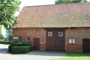 Heimatstube Wietzen Ziegelsteinbau mit Satteldach in Wietzen, Eingang mit Doppeltür, umgeben von grüner Hecke.