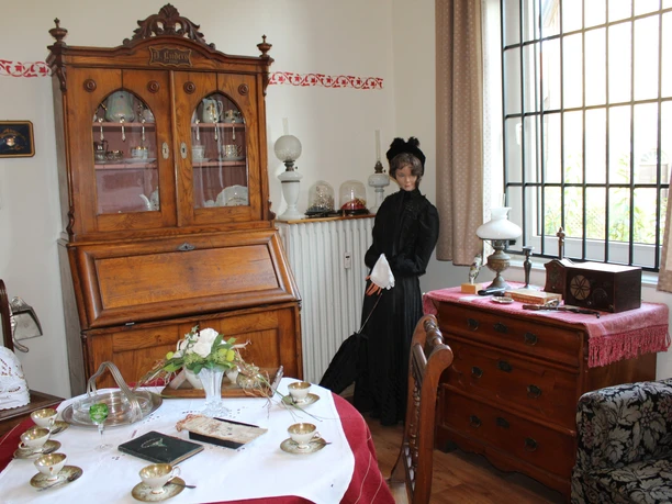 Ein historisch eingerichtetes Wohnzimmer mit antiken Möbeln und einer Figur in viktorianischer Kleidung.