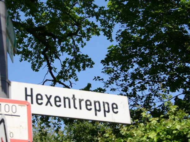 Hexentreppe Ein Schild mit der Aufschrift "Hexentreppe", umgeben von üppigem Grün und blauem Himmel im Hintergrund.